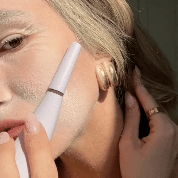 Using the Michael Todd Beauty Dermaplaning Essentials Kit, a person applies white powder to their cheek with an electronic beauty tool while supporting their face with one hand.
