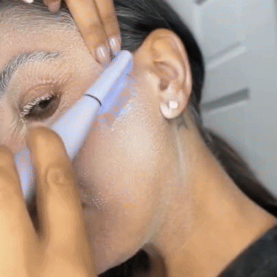 A person uses the Michael Todd Beauty Sonicsmooth Pro+ System to exfoliate facial skin, holding it at an angle near the cheek and ear for a smoother, more radiant complexion.