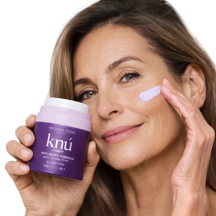 Woman applying cream to her face with a purple jar labeled 'knu' in front of a white background
