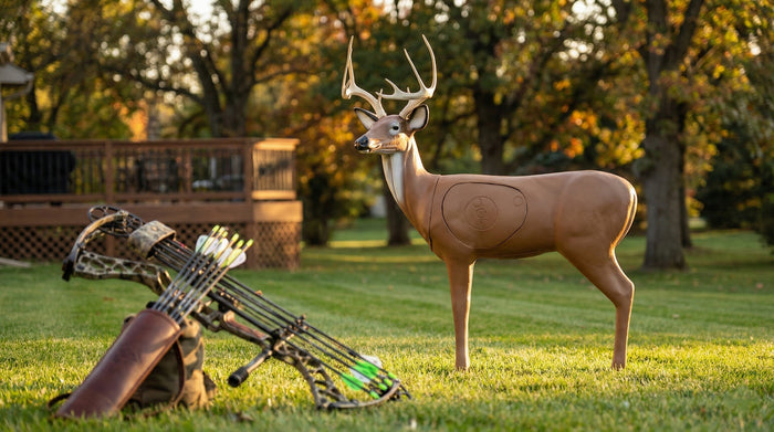 Archery bow and target deer stand on grass with trees in the background